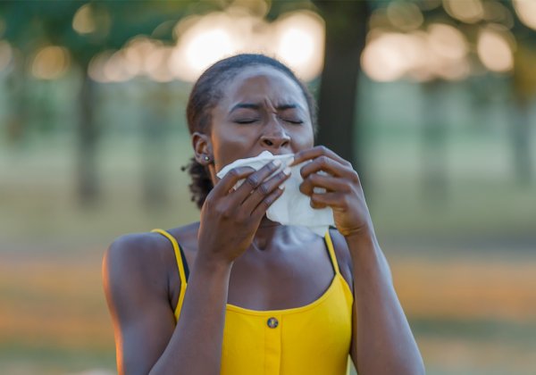 Woman in a yellow dress sneezing into a tissue
